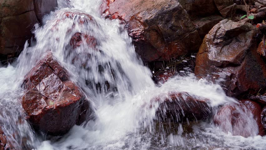 Close-up, clear melt water has found a way out and flows vigorously downstream through a crack in the rocks in a powerful stream, turning sharp stones into smooth boulders. Royalty-Free Stock Footage #1099171513