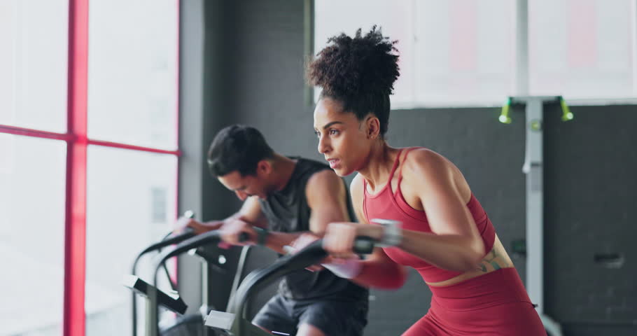 Determination, fitness and endurance with couple cycling in gym together for strength and stamina. Active, fit and bike cardio with african american friends cycle and ride for competitive exercising Royalty-Free Stock Footage #1099172055