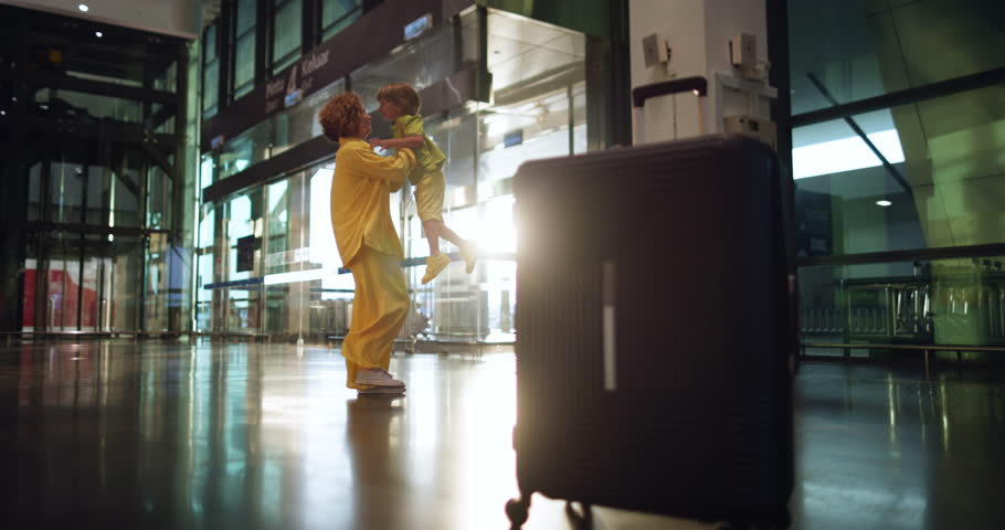 Luggage left in the foreground and a woman with a child in the background. Cinematic footage of a happy mother spinning with her son in her arms. A touching reunion of a friendly and strong family.  Royalty-Free Stock Footage #1099173253