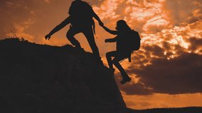 teamwork help business travel silhouette at sunset sunlight slow motion video concept. man and girl holds out a helping hand mutual assistance camping adventure a pair of hikers climb a mountain