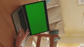 VERTICAL VIDEO, Young woman working on green screen chroma key laptop while sitting in apartment