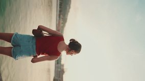 VERTICAL VIDEO: Close-up, girl stands on the embankment and looks at the bay. Young woman looks at the sea in the morning time. Back view