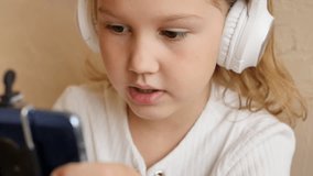 A cute teenage girl is talking on a video call using a phone and wearing headphones. Online education basic and additional. Distance learning using the Internet