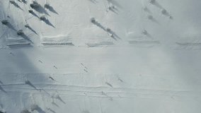 4k video footage of Snow-covered ski slope with skiers and snowboarders. People ski and snowboard in the snow - an aerial drone shot. People skiing slope on a frosty winter weather aerial drone shot.