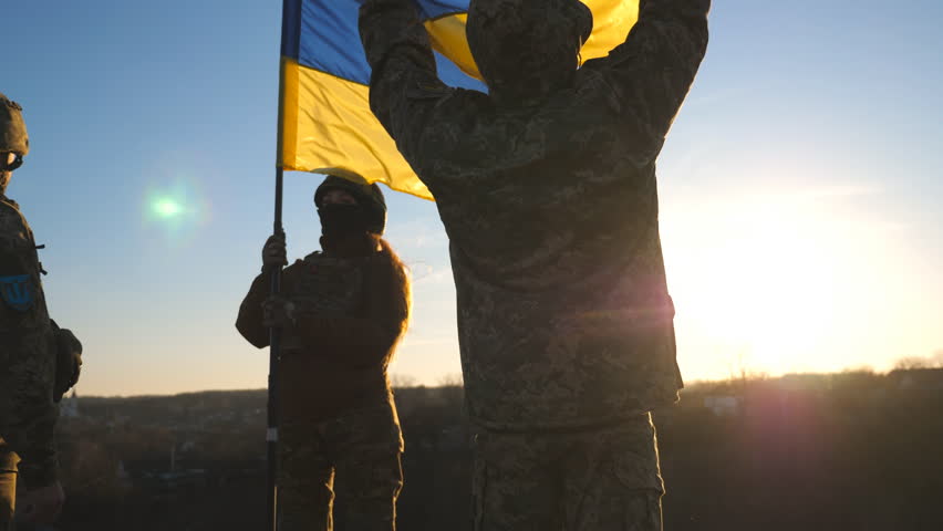 Soldiers of ukrainian army standing at top of hill and lifted up flag of Ukraine. People in military uniform holding waving flag as symbol of victory against russian aggression. End of war in Europe Royalty-Free Stock Footage #1099181697