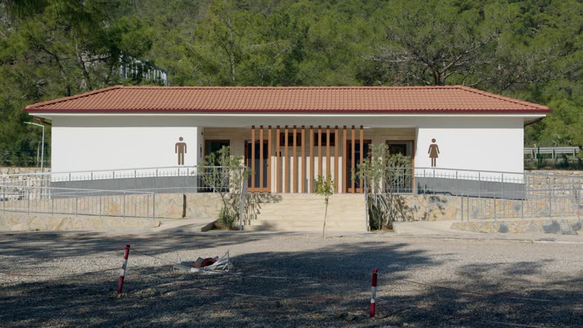 Toilet building with figures of man and a woman in black in city park. Separate building with WC rooms.