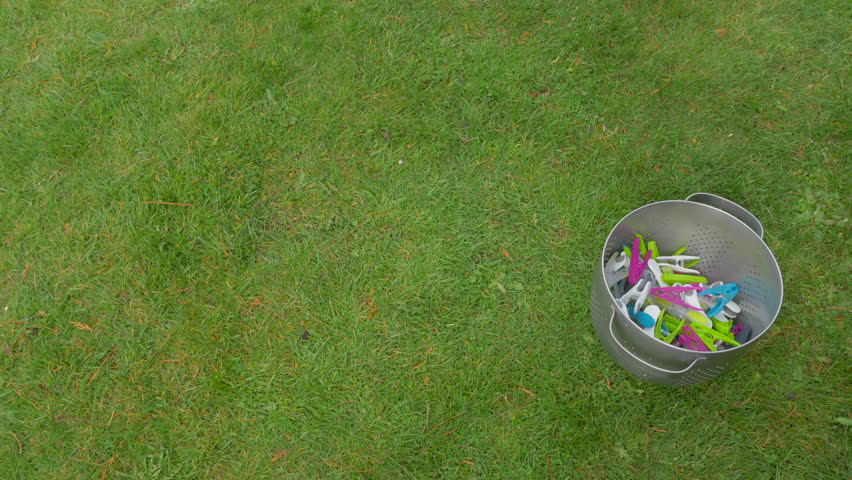 A man’s hand putting down a laundry basket full of wet washing, outside on grass next to a container of pegs, ready to hang out to dry.