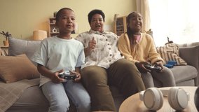 Two African American tween siblings and their modern grandmother playing video games together on couch in living room at daytime - Powered by Shutterstock - Get 15% off with code: PIKWIZARD15