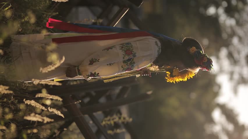 A beautiful Ukrainian girl in a Ukrainian national vyshyvanka dress with a bouquet of sunflowers against the background of anti-tank hedgehogs. war in Ukraine. War of Russia against Ukraine.