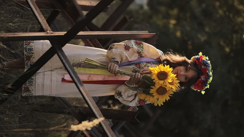 A beautiful Ukrainian girl in a Ukrainian national vyshyvanka dress with a bouquet of sunflowers against the background of anti-tank hedgehogs. war in Ukraine. War of Russia against Ukraine.