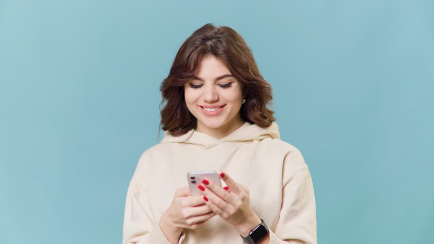 A teenage girl in a studio shot, She holds a smartphone in her hand and makes a satisfied | Shutterstock HD Video #1099196997