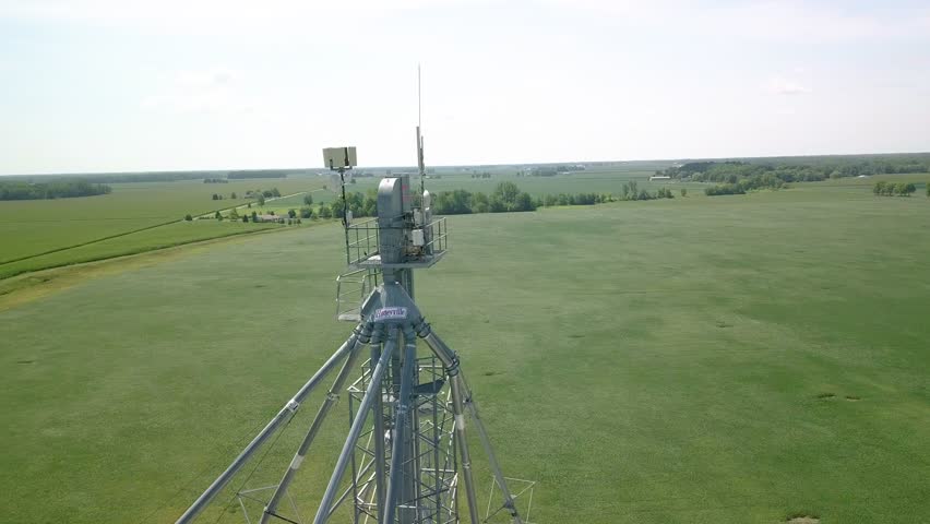 Aerial view orbiting weather measuring equipment and communications tower antenna overlooking rural Indiana farmland