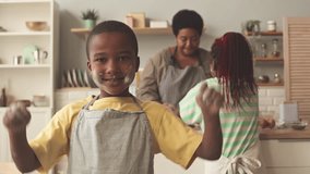 Portrait of little African American boy with flour on his face and in apron posing for camera while helping grandma and elder sister at kitchen - Powered by Shutterstock - Get 15% off with code: PIKWIZARD15