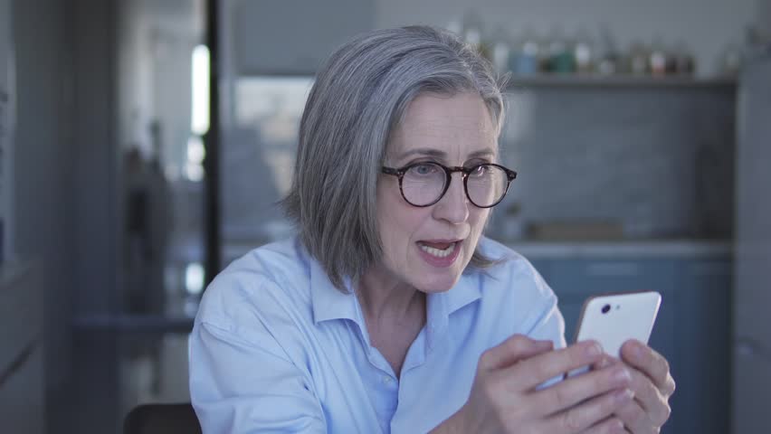 Serious woman boss with gray hair checking report of her employees on smartphone and going crazy through mistakes in work and incompetent execution of assignments and duties | Shutterstock HD Video #1099205673