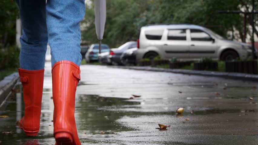 Woman in bright orange rain boots running in city, back view. Camera moving after her, tilting up and panning right Royalty-Free Stock Footage #1099208603