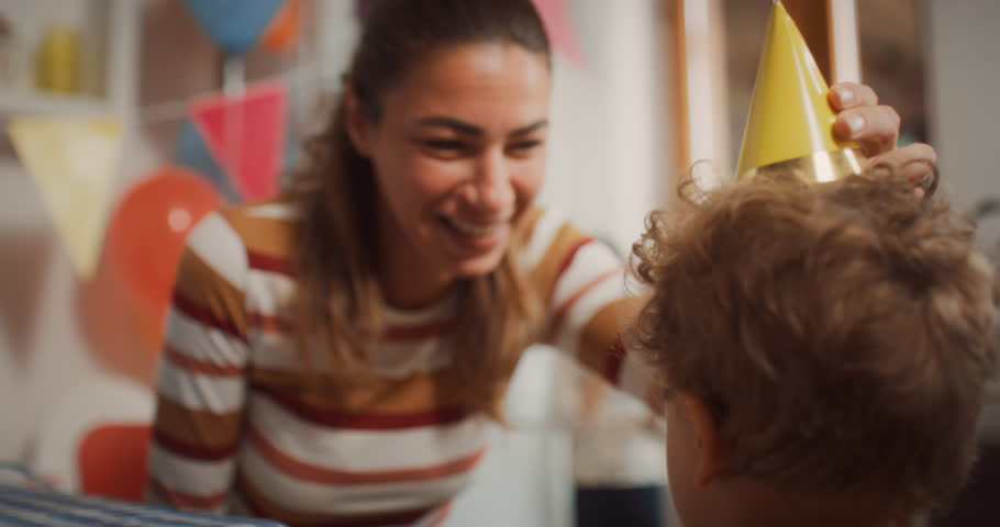 Authentic Shot of a Cheerful Mother Preparing a Party Hat for her Son for his Birthday in a Decorated Kitchen. Excited Young Woman Making a Colourful DIY Cone Hats for her Children | Shutterstock HD Video #1099208777