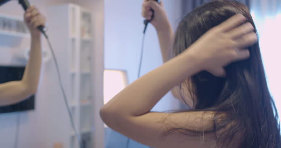 Beautiful woman Asian holding and using hot blow-dryer to long black hair in front of the mirror after taking a shower in morning.Routine lifestyle of female take care of hair health at home. Royalty-Free Stock Footage #1099210135