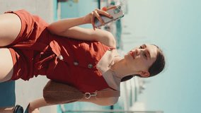 VERTICAL VIDEO: Сlose-up beautiful young woman sitting in the seaport uses a mobile phone. Сloseup portrait of girl looks into a smartphone on background yachts and ships