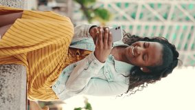 VERTICAL VIDEO, Closeup of young woman with long curly hair using mobile phone in an urban city background. Close-up of girl browsing social networks, shopping online