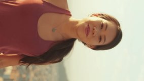 VERTICAL VIDEO: Young smiling woman crossing her arms and looking at the camera while standing on the observation deck