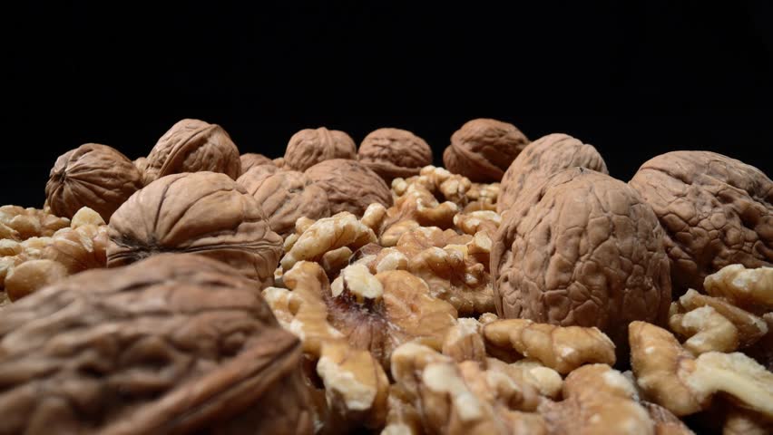Lots of whole walnuts in extreme macro shot. On a black background. Forward movement
