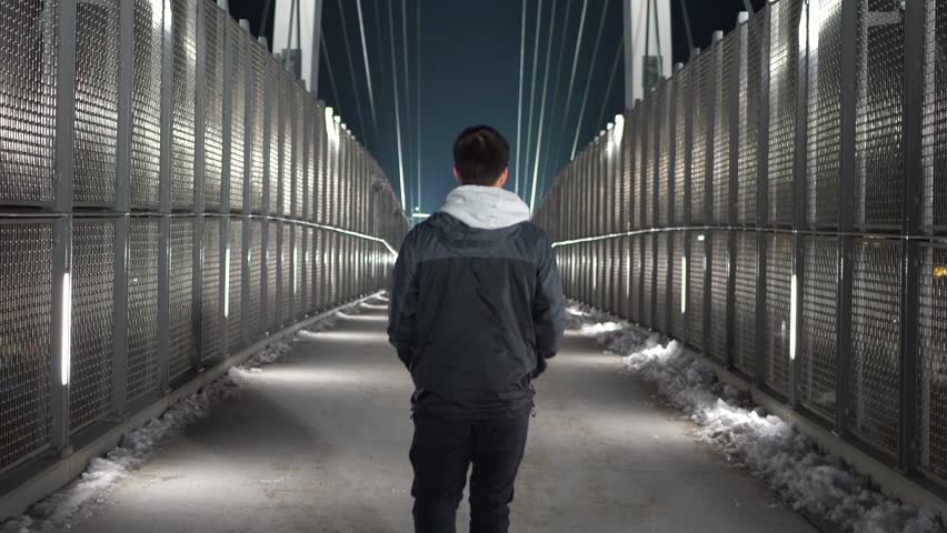 Young white male walking away from camera on a pedestrian bridge at night Royalty-Free Stock Footage #1099227267