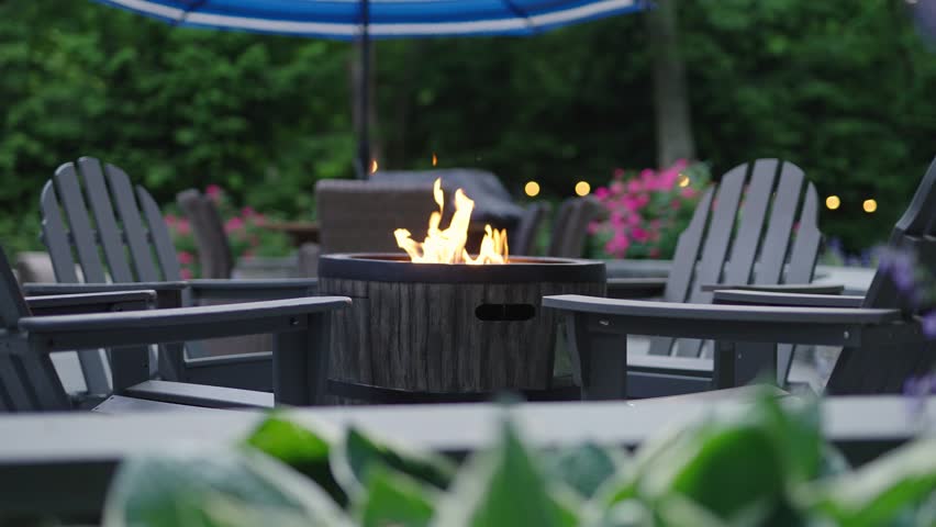 Gas outdoor fire pit on a patio. Outdoor living space with a fire pit and a garden. Royalty-Free Stock Footage #1099228621