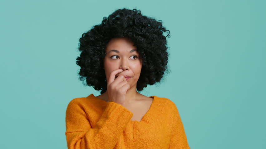 Bewildered confused dark skinned woman with afro hair has doubts and hesitation something. African American girl cant make right decision poses against blue background. Confused Afro American girl 4K | Shutterstock HD Video #1099231921