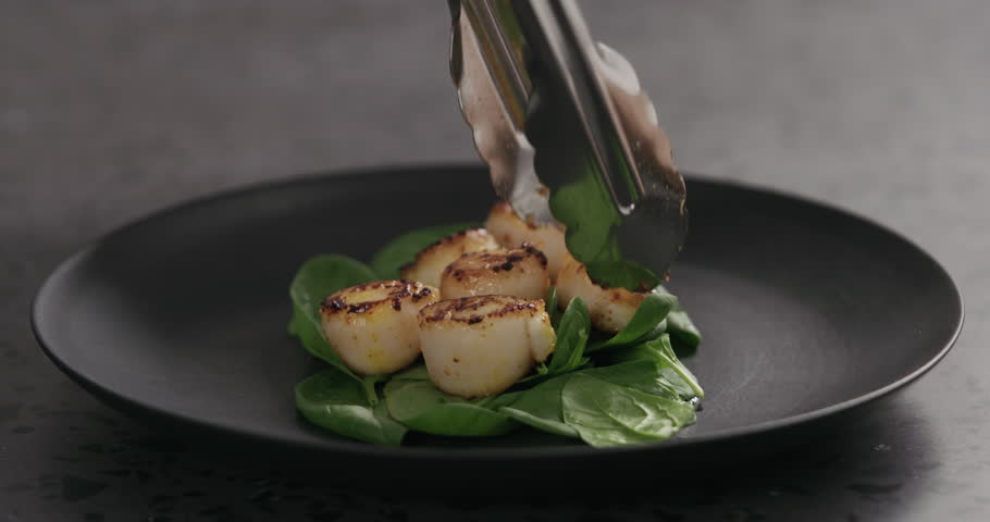 Slow motion put roasted scallops on spinach in black plate | Shutterstock HD Video #1099235967