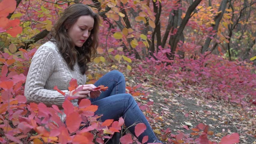 Portrait of pretty woman with maple leaves in her hand in an autumn park