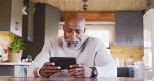 Happy senior african american man in log cabin, using smartphone for video call, slow motion. Free time, domestic life and communication concept.