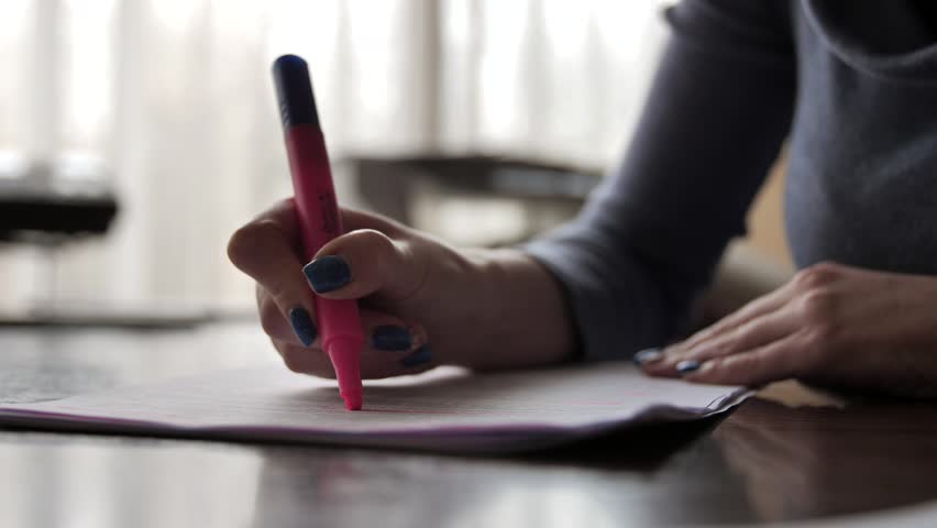 A woman highlights text in a document with a highlighter marker. Close-up of a felt-tip pen in female hands. Office worker works with documentation.