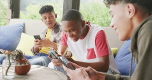 Video of happy diverse male teenage friends using smartphones, slow motion. Spending quality time at home together.