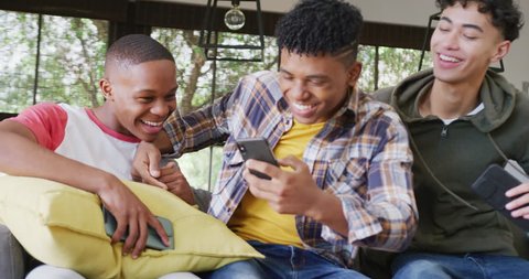 Video of happy diverse male teenage friends using smartphones, slow motion. Spending quality time at home together. Stock Video