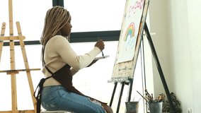 Female artist with brush and paint palette drawing rainbow in workplace art class - Powered by Shutterstock - Get 15% off with code: PIKWIZARD15