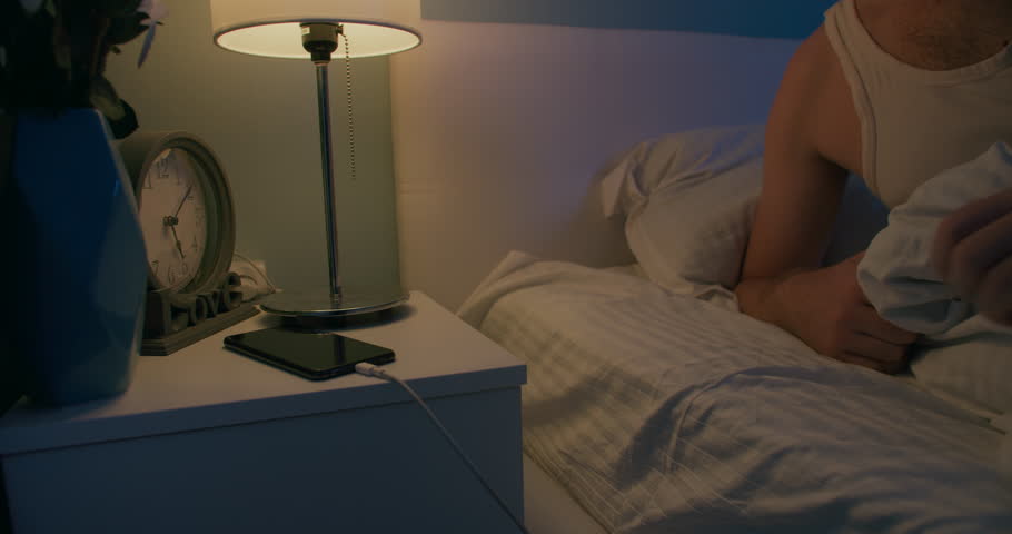 Young man put off eyewear and swith off light on nightstand and goes to sleep at night, medium close-up shot Royalty-Free Stock Footage #1099238525
