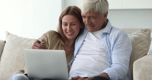 Senior father and pretty adult daughter watching movie on laptop at home, smiling, laughing, talking, discussing video content, enjoying online Internet communication, family relationships, bonding