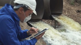 environmental pollution lifestyle radiation waste concept. man chemist scientist in a respirator mask studies water pollution digital tablet and an white helmet stands next to the waste pipes - Powered by Shutterstock - Get 15% off with code: PIKWIZARD15