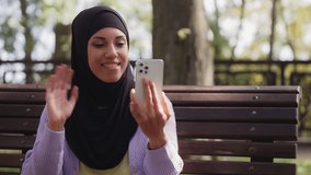 Middle-eastern woman in hijab waving hand on cellphone camera, online video call