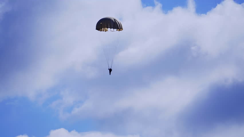 Silhouette of the man with parachute descending to the ground. Parachutist in blue cloudy sky.