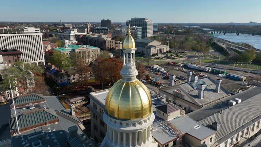Aerial orbit establishing shot of Trenton New Jersey State House dome. Delaware River and USA flag on winter day.
