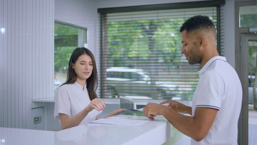 In a large modern clinic patient guy take his results on x-ray from the reception desk and go to the check appointment to the doctor Royalty-Free Stock Footage #1099246351