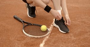 Young woman tennis player ties the laces on court