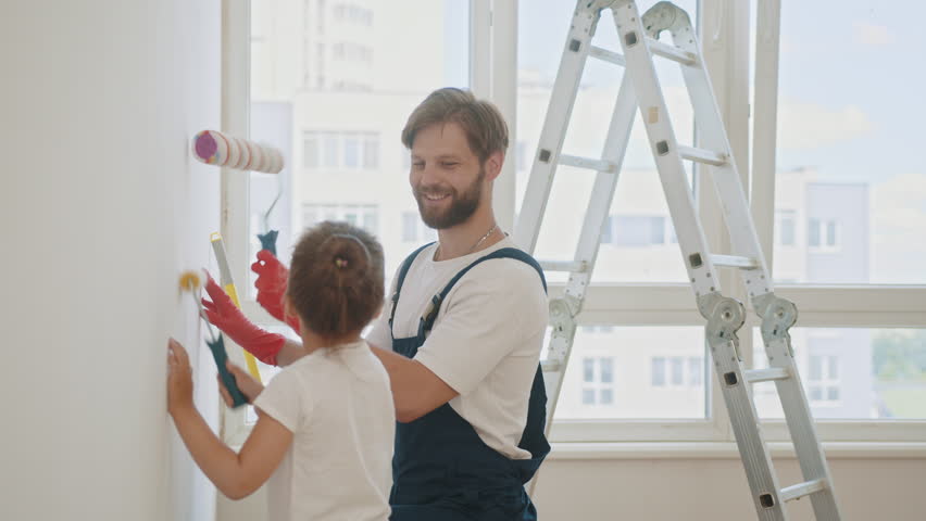 Father and his little daughter painting a wall in new home. Happy father teaching little adorable kid girl daughter how to paint wall using paint brush. Home renovation and repair concept Royalty-Free Stock Footage #1099252973