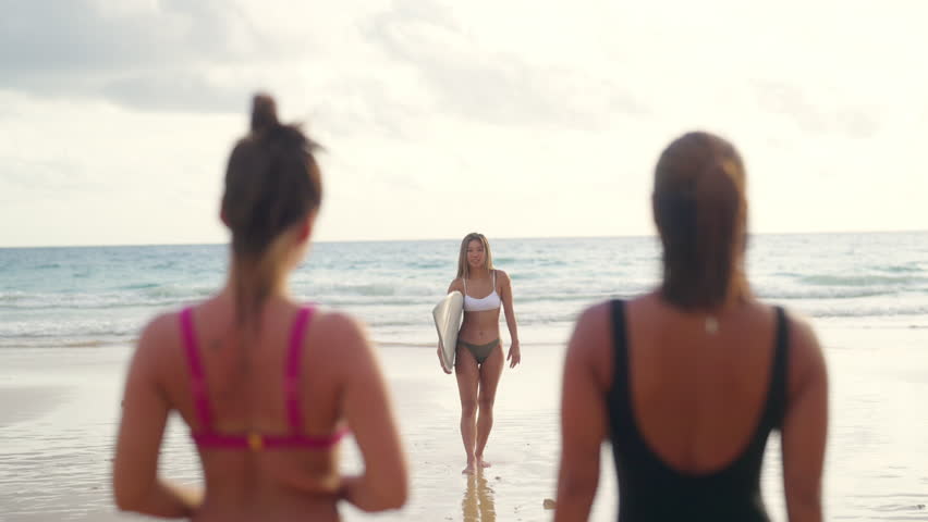 Asian woman surfer in bikini holding surfboard walking from the ocean on tropical beach in sunset. Attractive girl enjoy outdoor activity lifestyle water sport training with friends on summer vacation