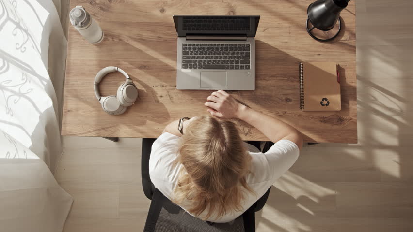 Girl at desktop, top down view, upset, disappointed, annoyed, takes her head with her hands in anger. Emotional burnout at work or home office. freelancer can not do job and pounding fists on table | Shutterstock HD Video #1099264123