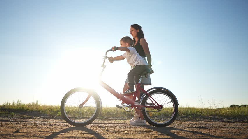 Mom teaches son to ride a bike. happy family childhood dream concept. mom and little son learn to ride a bike silhouette in the park in nature. happy family goes in for sports outdoors sunlight | Shutterstock HD Video #1099269079