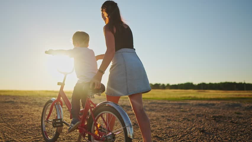 Mom teaches son to ride a bike. happy family childhood dream concept. mom and little son learn to ride a bike silhouette in the park in nature. happy family sunlight goes in for sports outdoors | Shutterstock HD Video #1099269085