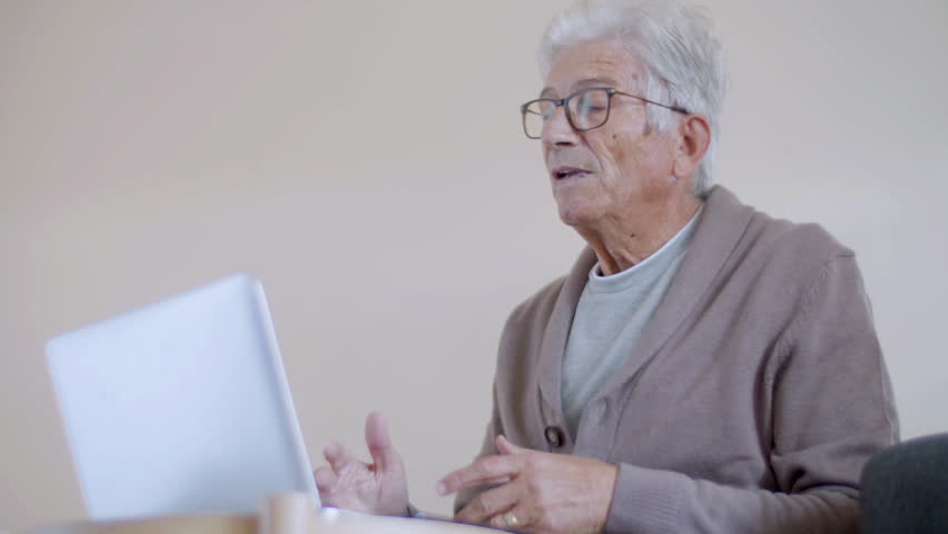 Senior man having video call with colleagues at home. Elderly man in eyeglasses sitting at table, looking at laptop screen, gesturing, discussing work issues. Communication, modern technology concept | Shutterstock HD Video #1099269181