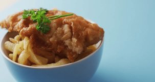 Video of fish and chips with parsley in bowl, on blue background